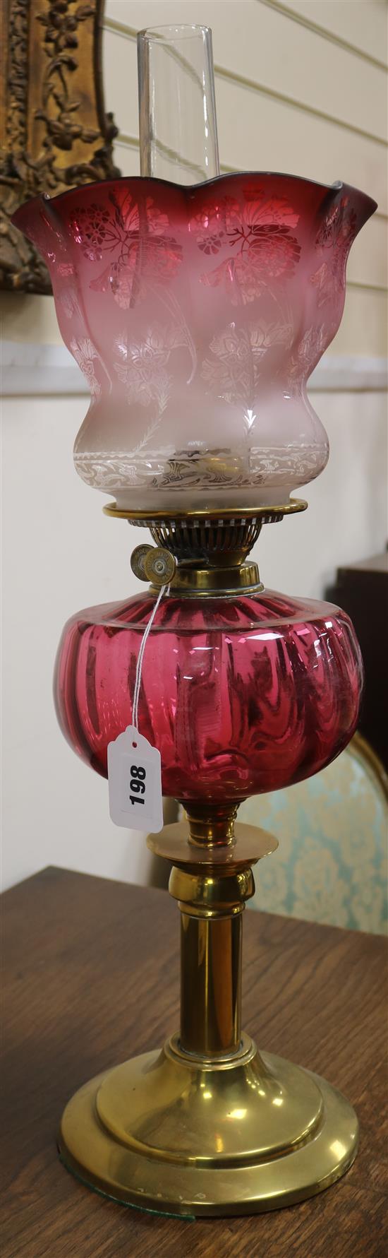 A cranberry glass oil lamp with cranberry shade and two others, smaller with shades